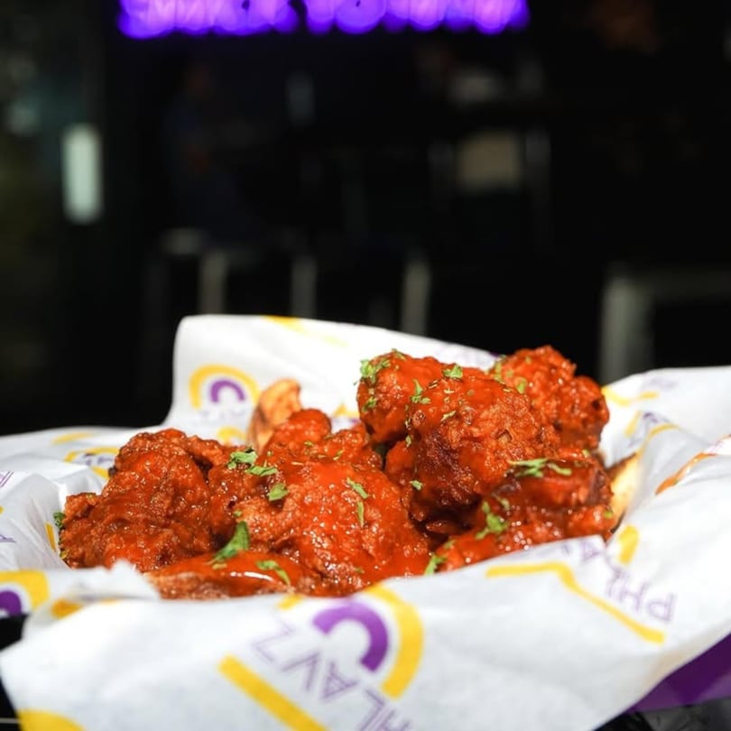 A basket of Phlavz Caribbean-style chicken wings, coated in red sauce and garnished with parsley.