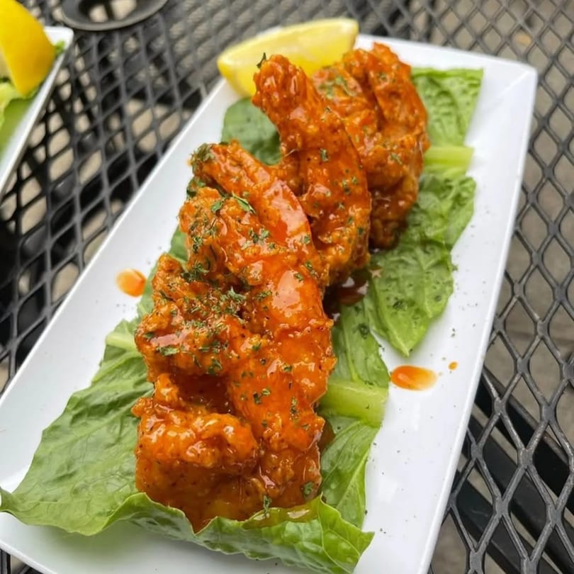 Phlavz Caribbean shrimp appetizer, coated in orange sauce, on a bed of lettuce with a lemon wedge.