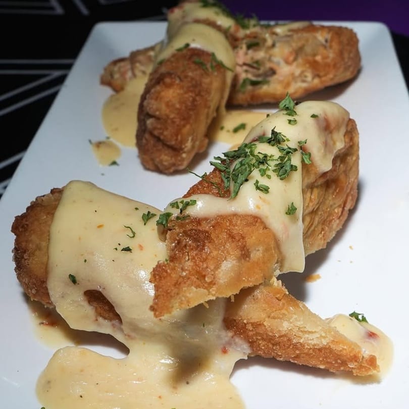 Crispy fried Caribbean fritters drizzled with a creamy sauce and garnished with fresh parsley on a white plate.