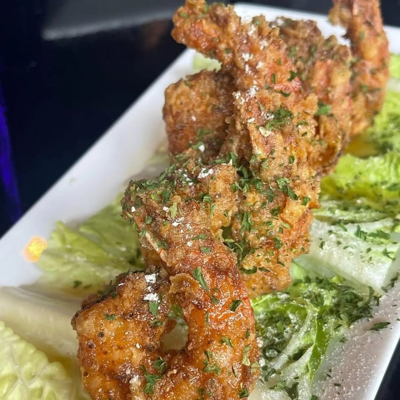Crispy fried shrimp, garnished with parsley and powdered sugar, served on a bed of fresh lettuce.