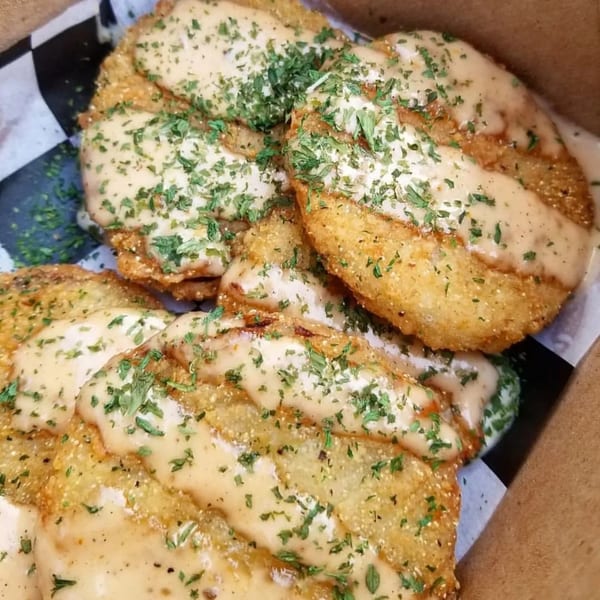 Golden-brown fried plantains topped with a creamy sauce and fresh parsley in a takeout box.