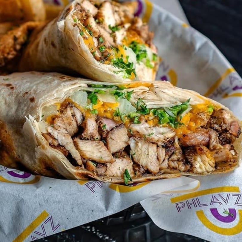 Two Phlavz Caribbean chicken wraps, cut in half, filled with meat, cheese, and greens.
