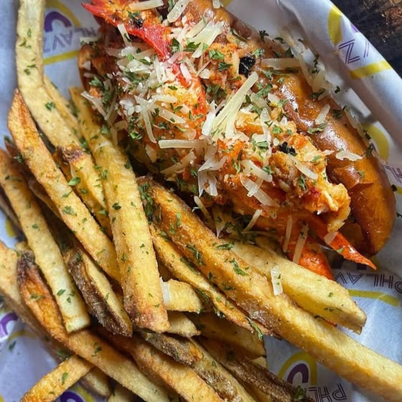 A Caribbean lobster roll with fries, garnished with cheese and herbs, served in a branded basket.